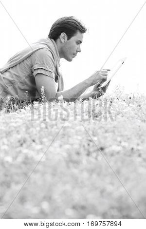 Side view of young man using digital tablet while lying on grass against clear sky