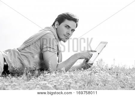 Side view of young man using digital tablet while lying on grass against clear sky