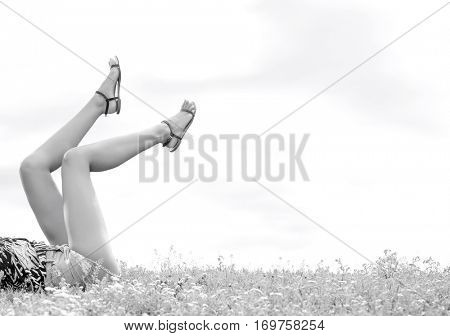 Low section of woman with feet up lying on grass against sky