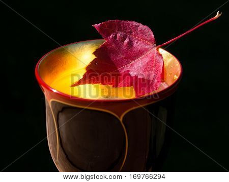 Red maple leaf in a wooden wine cup against black background