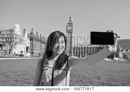 Young woman taking self portrait through smart phone against Big Ben at London; England; UK