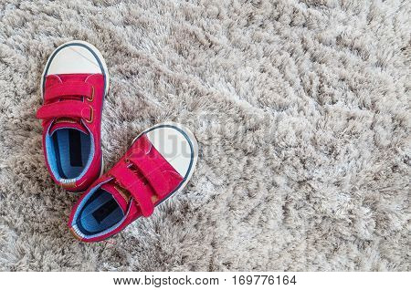 Closeup red fabric sneakers of kid on gray carpet textured background in top view with copy space