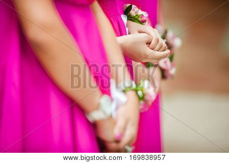 Bridesmaids in bright pink dresses standing in row with bracelet boutonnieres on hands. Woman friends of bride at wedding party. Girls in identical gown, close up of hands with decorative elements