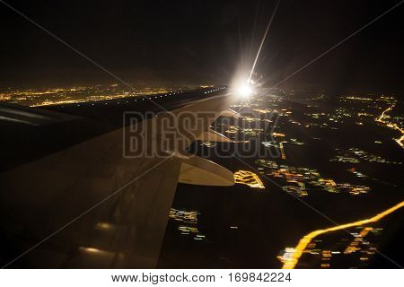 Aerial view of night city landscape. Earth viewed from airplane under aircraft wing. Lights of modern city from the bird fly