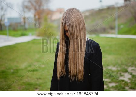 Blond girl with long blonde hair covering her face in the park