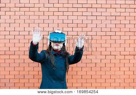 Handsome young woman using VR glasses with brickwall background and space for text
