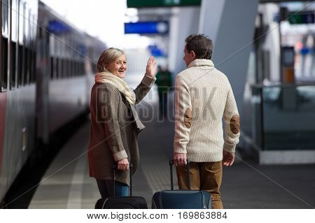 Beautiful senior couple on trainstation pulling a trolley luggage. Rear view.