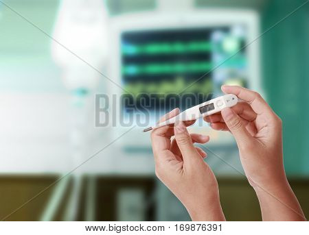Close up of thermometer showing high temperature in woman hand with drop of saline solution and medical monitors blurred background Temperature measuring by a thermometer Fever measuring.