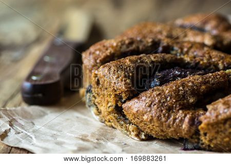 Homemade eggless plum cake on parchment paper, knife, close up selective focus, cozy rustic kitchen interior