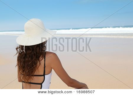 ผู้หญิงสวยงามนั่งอยู่บนชายหาดกับหมวกฟาง