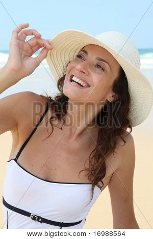 ผู้หญิงสวยงามนั่งอยู่บนชายหาดกับหมวกฟาง