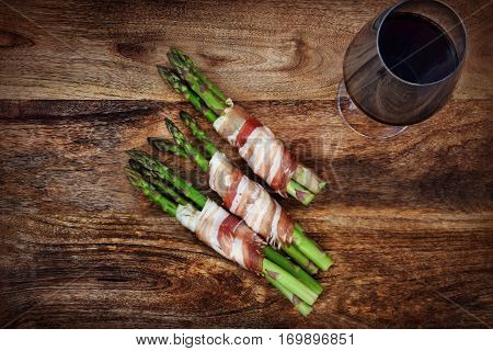 Green asparagus with bacon and a glass of red wine on a dark rustic wooden table