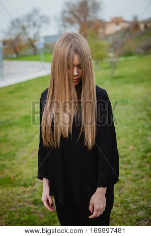 Blond girl with long blonde hair covering her face in the park