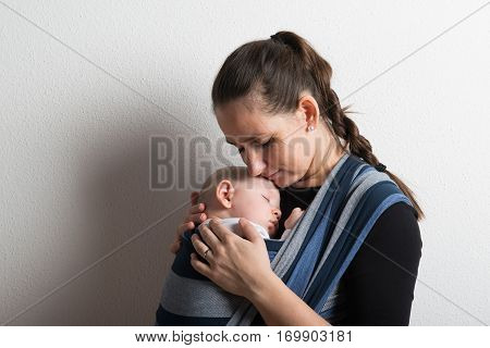 Beautiful young mother with her baby son sleeping in sling. Studio shot on white background.