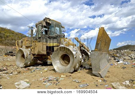 A huge tractor with a front end loader and metal wheels is used to move trash in a city dump