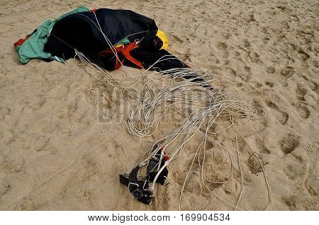 A parasail and harness are left on a sandy beach awaiting the next rider.