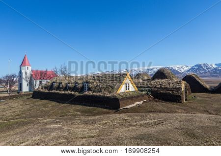 Historic turf-roofed farmhouses built with peat. The sod houses are flanked by a church while the background shows the mountain range around Olafsfjordur. Glaumbaer Varmahlid Iceland.