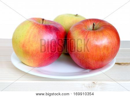 Three big ripe apples on white palte in wooden shelf on white background front view closeup