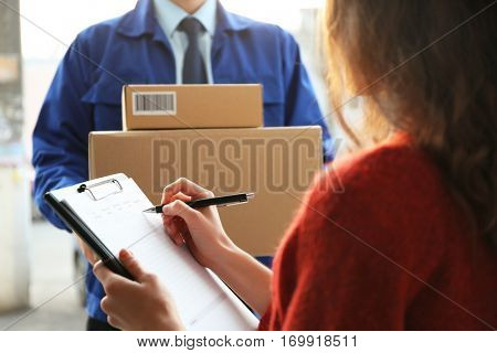 Young woman signing documents after receiving parcels from courier, closeup