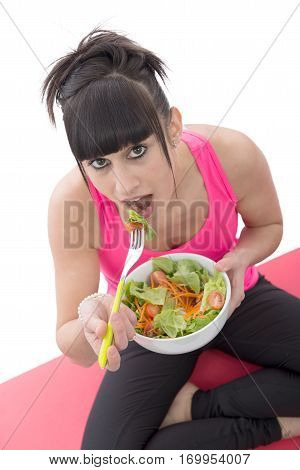 A young brunette sporty girl eats salad
