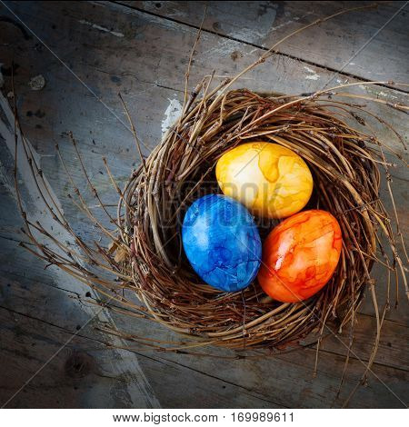 Colorful easter eggs in a nest from straw on a old shabby wooden table