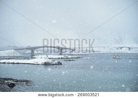 Fredvang bridges in heavy snowfall in winter with fishing ship. Lofoten islands, Norway