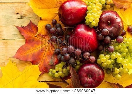 Top View On Red Juicy Ripe Apples With Grapes And Autumn Maple Leaves On A Wooden Background