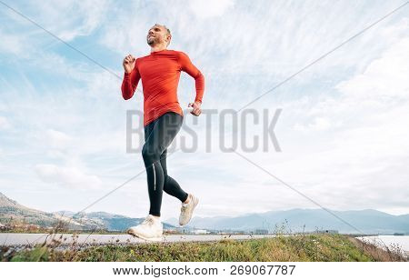 The Wide Angle Shoot Of A Man Dressed In Red Long Sleeve Shirt Runs By The Road With Mountain Backgr