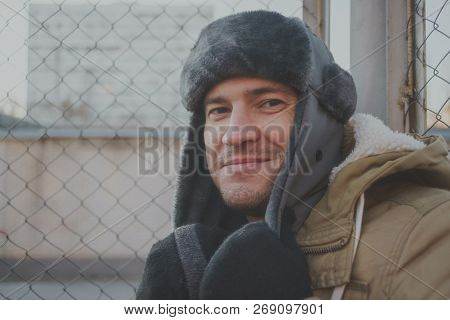Happy Handsome Young Man In Cap With Earflaps. The Young Man In The Fur Hat. A Young Guy Standing On