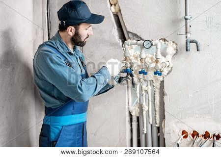 Workman In Blue Uniform Installing Water Heating System On The Construction Site Of A New House