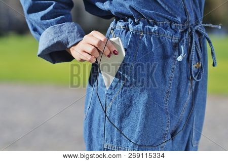 A Girl In A Denim Suit Pulls Out A Smartphone To Listen To Music. Spring Sunny Day The Warmth
