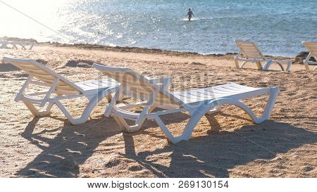 Two Plastic White Sunlongers On The Sand Beach Near The Sea.