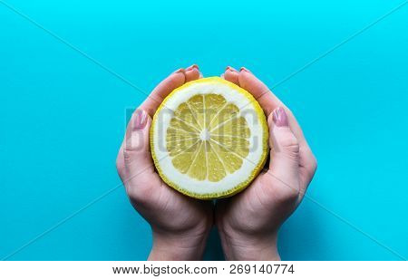 Hand Of A Girl Holds A Half Big Lemon On A Blue Background. Flat Lay Closeup Top View