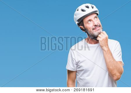 Middle age senior hoary cyclist man wearing bike safety helment isolated background with hand on chin thinking about question, pensive expression. Smiling with thoughtful face. Doubt concept.