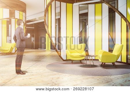 Businessman Standing In Modern Office Waiting Area With Gray Walls, Wooden Floor, Yellow Door And Ye