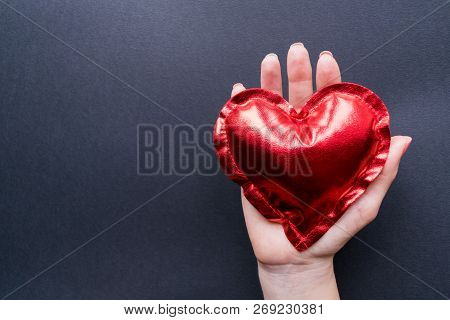 Love Concept. Valentine`s Day. The Hand Of A Girl Holds A Red Heart On A Dark Background. Flat Lay T