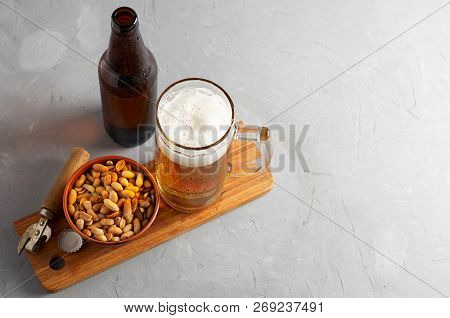 Lager Beer Pouring In Glass And Bottle With Salted Peanuts On Gray Concrete Background