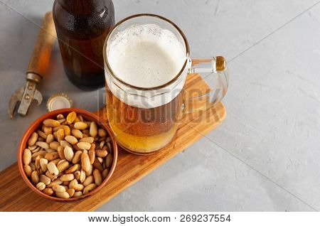 Lager Beer Pouring In Glass And Bottle With Salted Peanuts On Gray Concrete Background