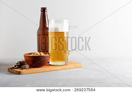 Lager Beer Pouring In Glass And Bottle With Salted Peanuts On Gray Concrete Background