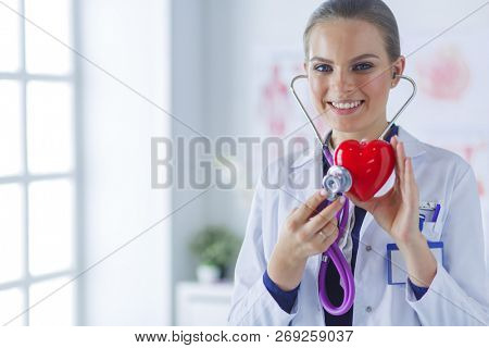 A doctor with stethoscope examining red heart, isolated on white background