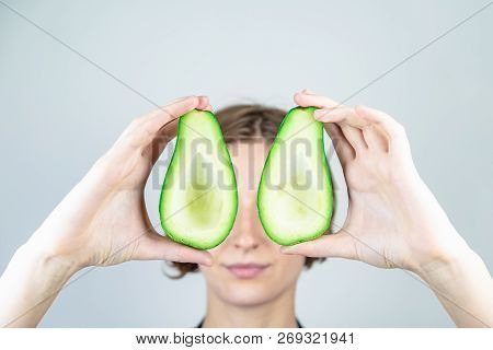 Fresh Ripe Avocado In Woman Hands. Female Face Hidden Behind Halves Of Avocado Fruit In Studio Backg