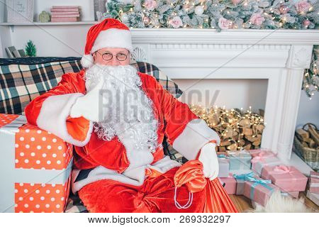 Nice Man Wears Santa Claus Costume And Whhite Beard. He Sits And Looks On Camera. Guy Shows Big Thum