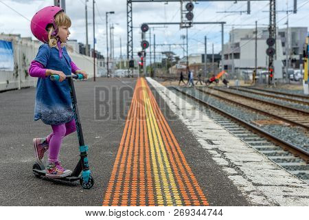 Young Girl In Pink Outfit And Pink Helmet Riding A Kick-scooter Across The Railway Line