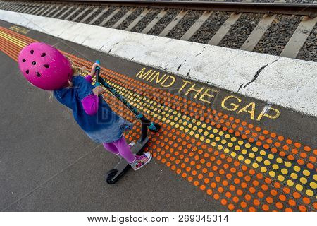Young Girl In Pink Outfit And Pink Helmet Riding A Kick-scooter Across The Railway Line