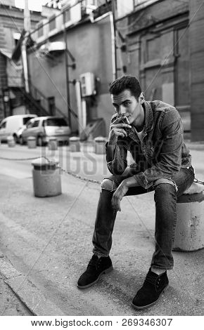 Black And White Photo Of Charismatic Boy In Jeans Jacket Smoking On The Street.