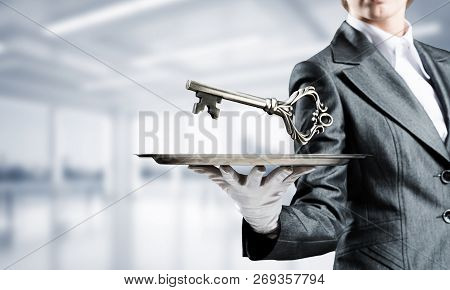 Cropped Image Of Waitresss Hand In White Glove Presenting Big Key On Metal Tray With Office View On 