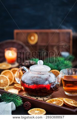 Glass Teapot Of Hot Black Tea On Cozy Background With Dried Oranges And Candles