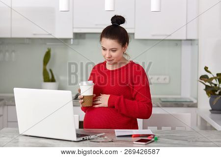 Pregnancy And Work Concept. Pretty Lady Has Hair Knot, Wears Red Sweater, Holds Takeaway Coffee, Kee