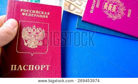 Hands Holding Passports On Blue Background. Citizenship Of Estonia And Russia. Citizenship Of Europe