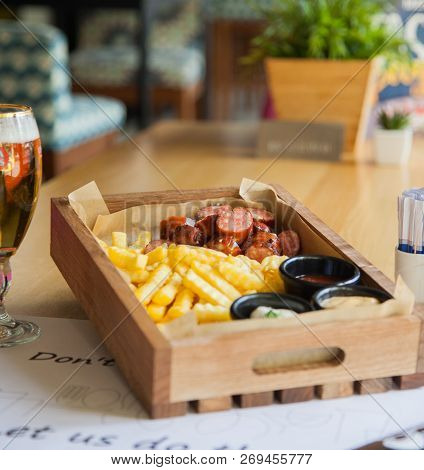 Delicious Smoked Sausage With Chips, French Fries With Sauce On Wooden Board. Street Fast Food Festi